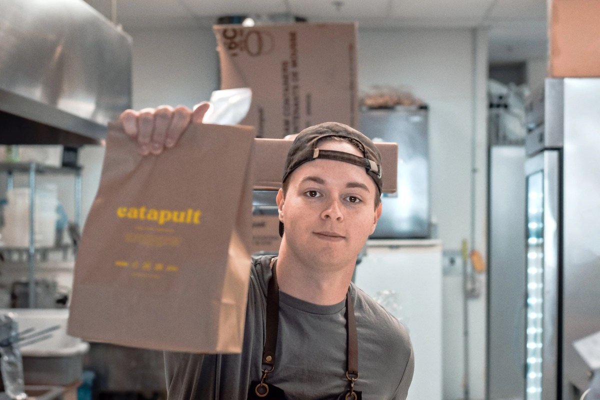 A kitchen worker holding a Catapult-branded takeout bag